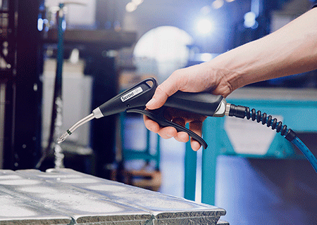 A hand holding the air blow gun SILVENT Pro One in a manufacturing industry, pointing it downwards.