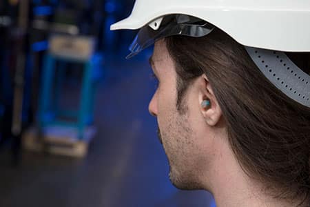 Close-up of a factory worker equipped with a helmet and earplugs for safety.