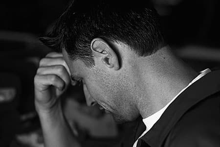 Man in a factory holding his forehead in pain, experiencing a hearing-related injury.