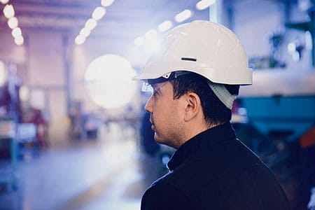 A worker wearing a white helmet in a blue-lit industrial environment.